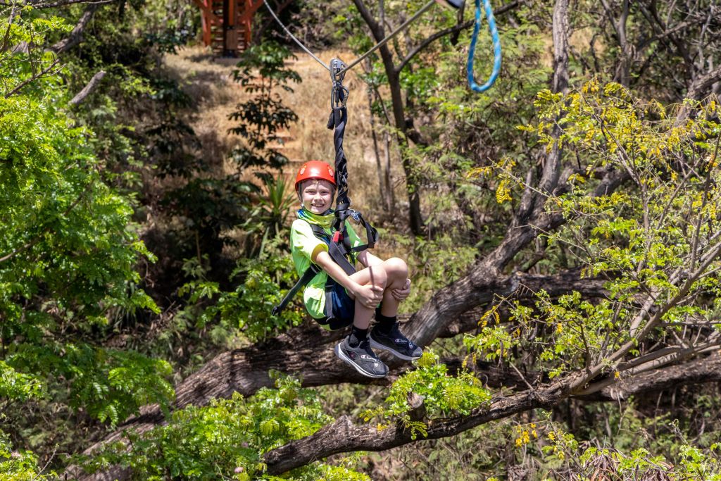 숲 사이로 빨간 헬멧과 초록색 셔츠를 입은 아이가 미소를 짓고 있습니다.
