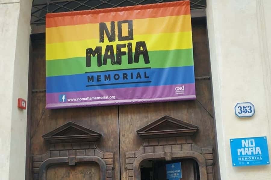 나무 문 위에 무지개 디자인과 웹 사이트 nomafiamemorial.org를 특징으로하는 다채로운 "No Mafia Memorial" 배너.