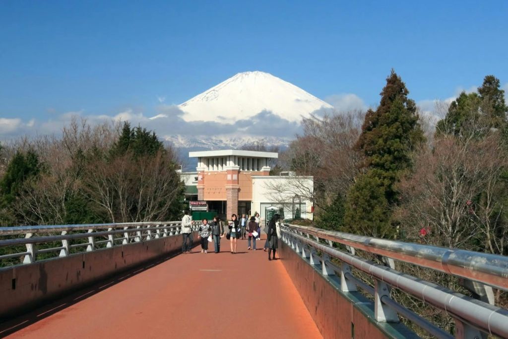 맑은 날 후지산을 배경으로 붉은 보행자 다리를 걷는 한 무리의 사람들.