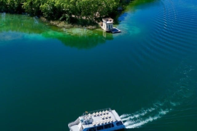 빽빽한 나무와 작은 석조 구조물이 있는 작은 섬 근처의 잔잔한 호수를 가로질러 이동하는 보트의 공중 풍경.