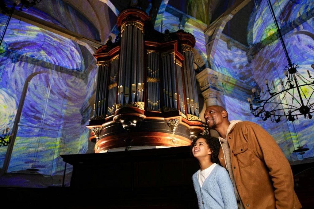 벽과 천장에 화려한 예술적 투영이 있는 조명 인테리어의 커다란 파이프 오르간을 감상하는 두 사람.
