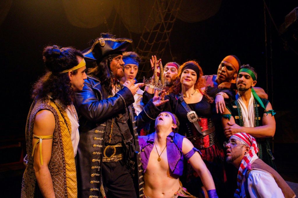 해적 의상을 입은 한 무리의 사람들이 왕관을 들고 있는 남자 주위에 모여 흥분과 호기심을 표현합니다.