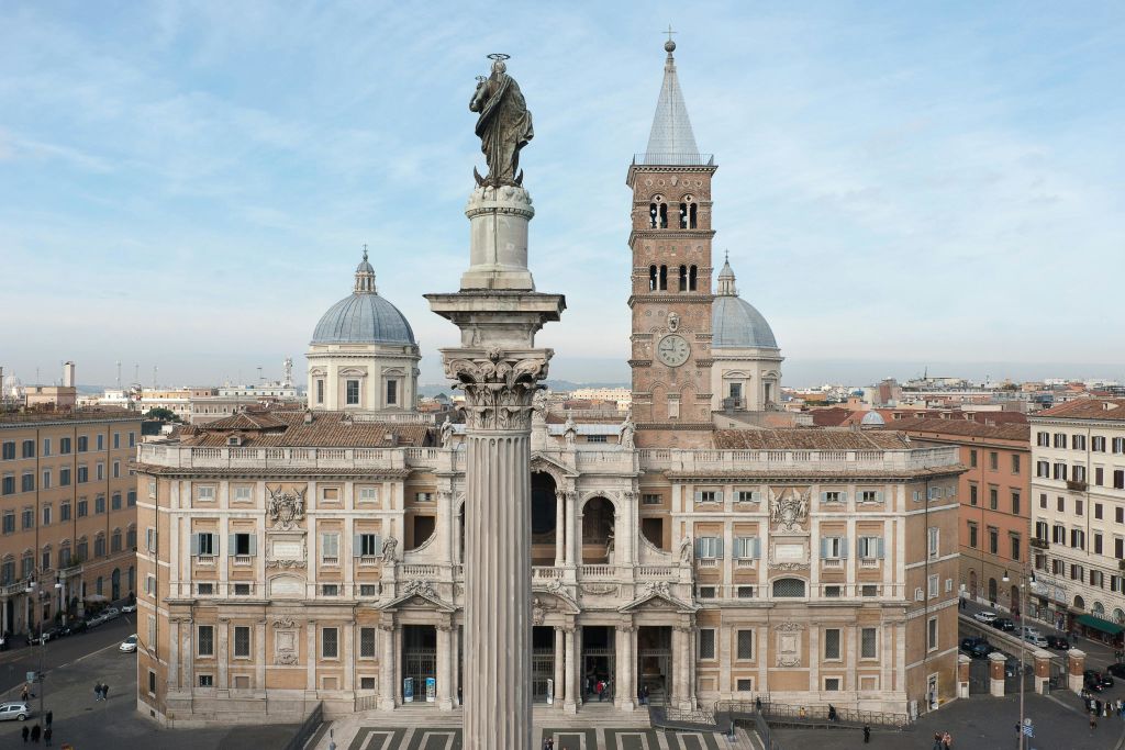 두 개의 돔과 시계탑이 있는 웅장하고 유서 깊은 건물로, 앞에 동상이 놓인 높은 기둥이 있습니다.