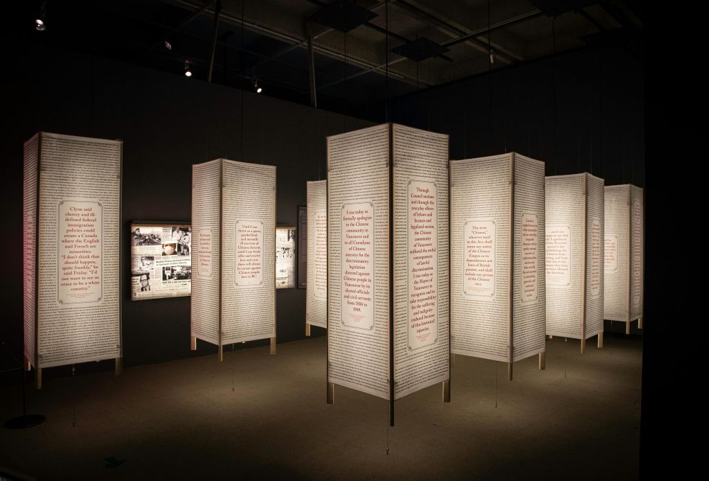 조명이 희미한 방에서 텍스트 패널을 걸고 전시하세요. 배경에는 역사적인 사진이 있는 조명 보드가 보입니다.