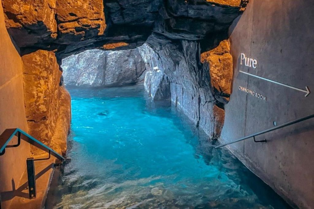 오른쪽 벽에 탈의실 표지판이 있는 바위 동굴 내부의 맑고 푸른 수영장.