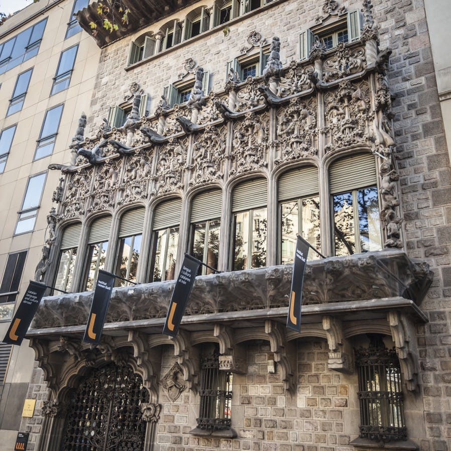 커다란 아치형 창문, 정교한 조각, 창문 아래에 매달린 검은색 배너가 있는 화려한 석조 건물 외관.