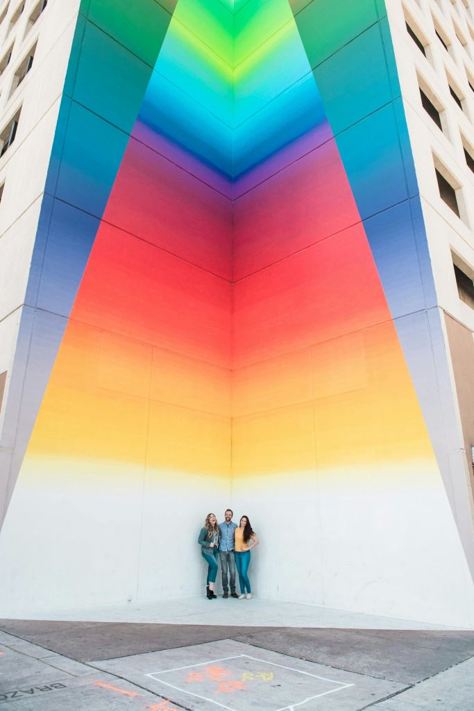 건물 모퉁이에 그려진 활기차고 다양한 색상의 벽화 앞에서 세 사람이 포즈를 취하고 있습니다.