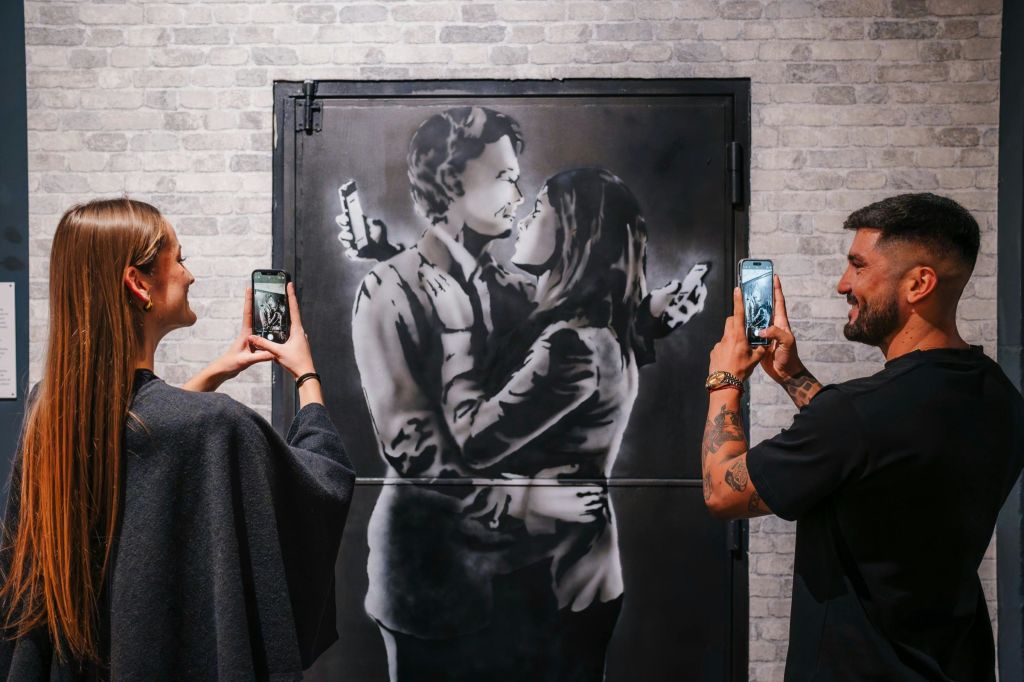 한 커플이 뱅크시 벽화의 합동 사진을 찍고 있습니다.