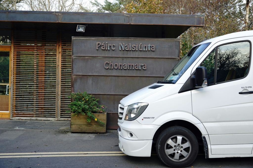 흰색 밴은 "Páirc Naisiúnta Chonamara" 라고 적힌 표지판과 푸른 단풍이 있는 화분이 있는 건물 앞에 주차했습니다.