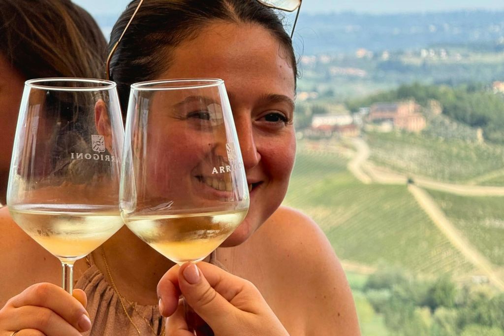 토스트와 포도밭 풍경을 배경으로 화이트 와인 한 잔을 들고 미소를 짓고 있는 여성.