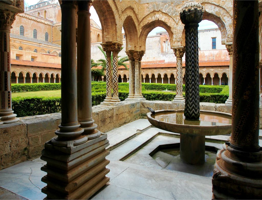 정교하게 조각된 아치와 기둥, 잘 다듬어진 울타리로 둘러싸인 중앙 분수가 있는 유서 깊은 안뜰.