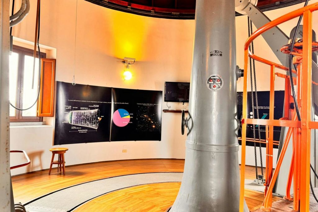 커다란 망원경이 유익한 포스터와 벽에 노란색 조명이 있는 원형의 방에 서 있습니다.