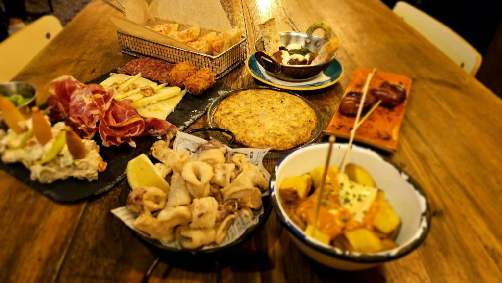 칼라마리 튀김, 세라노 햄, 치즈, 초리조, 감자 웨지, 프리타타 등 나무 테이블에 놓인 다양한 타파스.