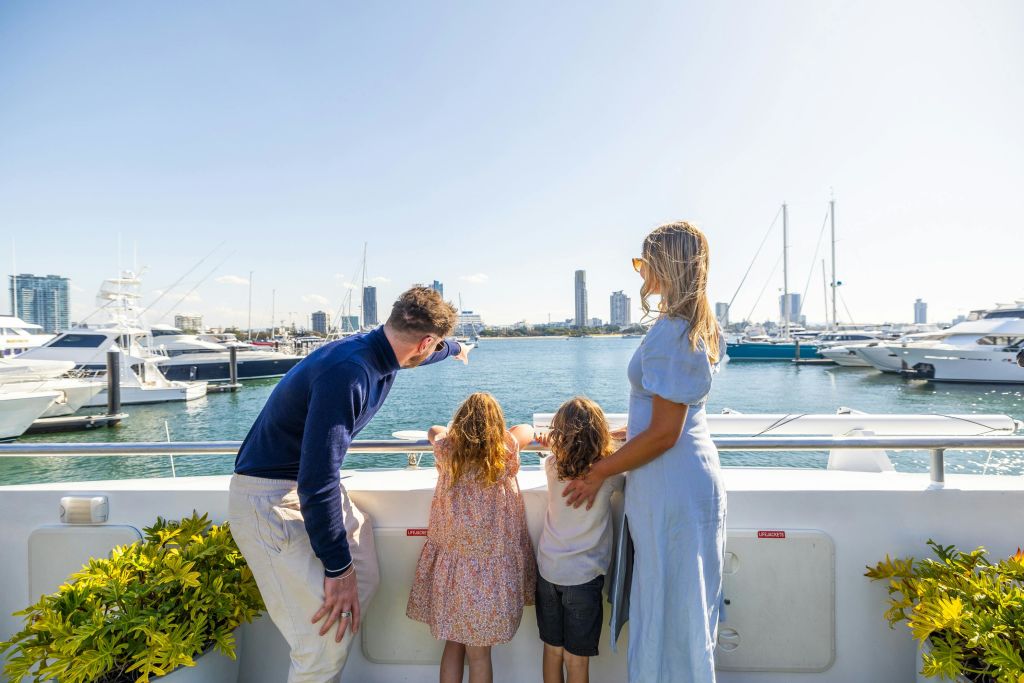 높은 빌딩을 배경으로 4인 가족이 배를 타고 정박지를 내려다보고 있습니다. 아버지는 바닷가를 가리켰다.