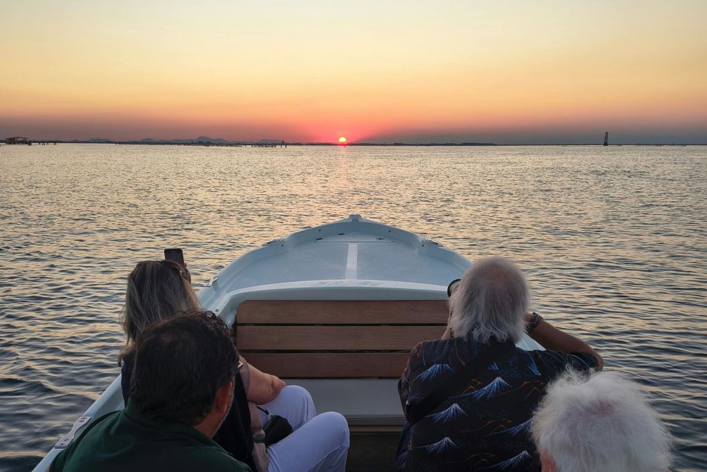 보트를 탄 승객들은 평온한 물 위로 지는 석양을 바라보며, 수평선은 낮고 맑은 하늘을 감상할 수 있습니다.
