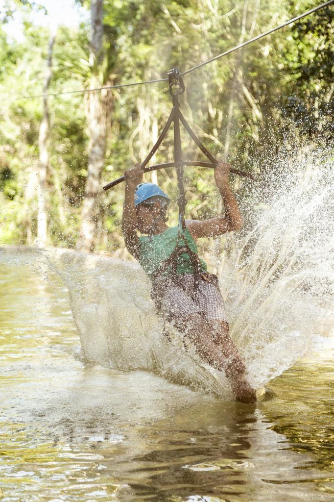 파란색 헬멧과 녹색 셔츠를 입은 사람이 물 위로 지퍼 라이닝을 입고 나무를 배경으로 커다란 스플래시를 연출합니다.