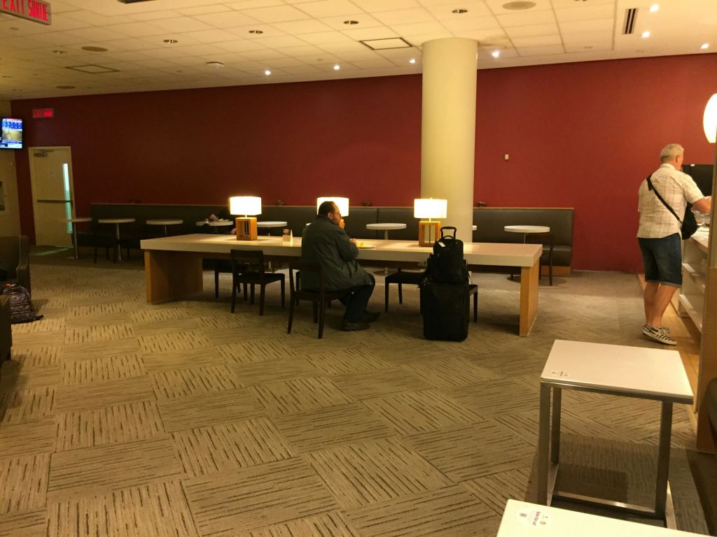 한 사람이 램프가 있는 커다란 테이블에 홀로 앉아 넓고 카펫이 깔린 라운지 공간의 적갈색 벽을 마주하고 있습니다.