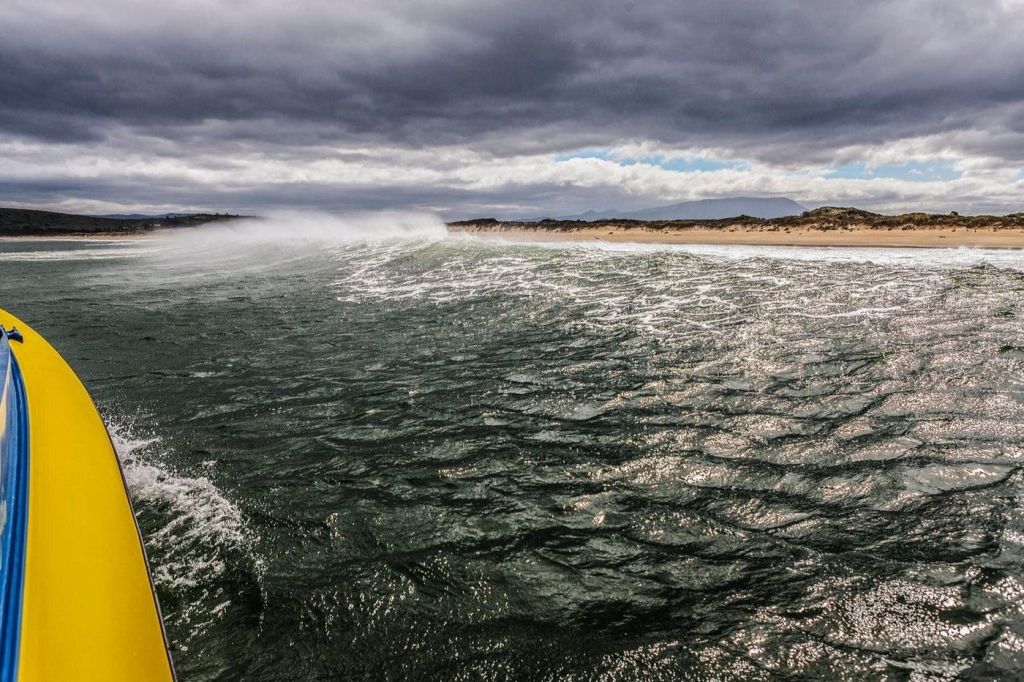 바닷가를 따라 먼 모래 언덕이 흐린 하늘 아래 어둡고 물결치는 바닷물.