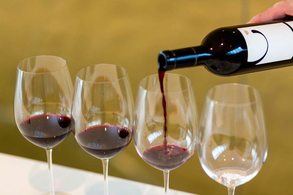 레드 와인은 병에서 네 개의 와인 잔 중 하나에 부어지고 일부 잔은 부분적으로 채워집니다.