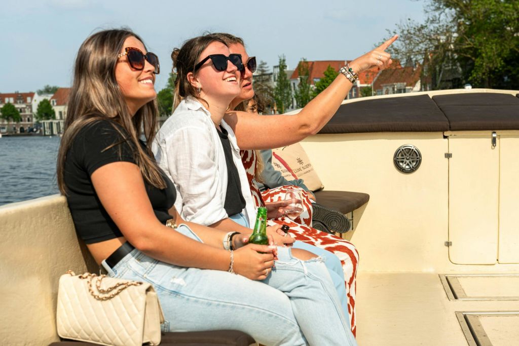 세 명의 여성이 보트에 앉아 미소를 짓고 화창한 날을 즐기고 있으며, 물과 건물이 배경으로 보입니다.