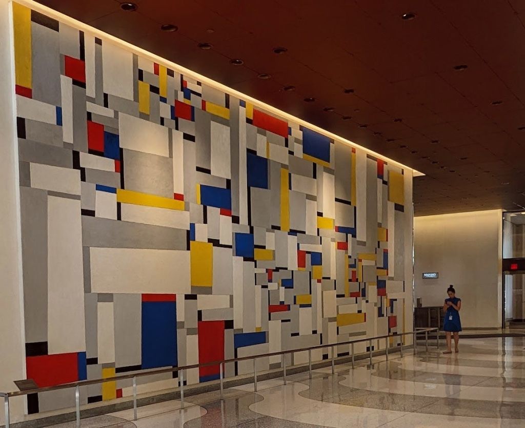 현대적인 실내 공간에 화려한 기하학적 모양의 격자가 있는 커다란 벽 벽화로, 근처에 사람이 서 있습니다.