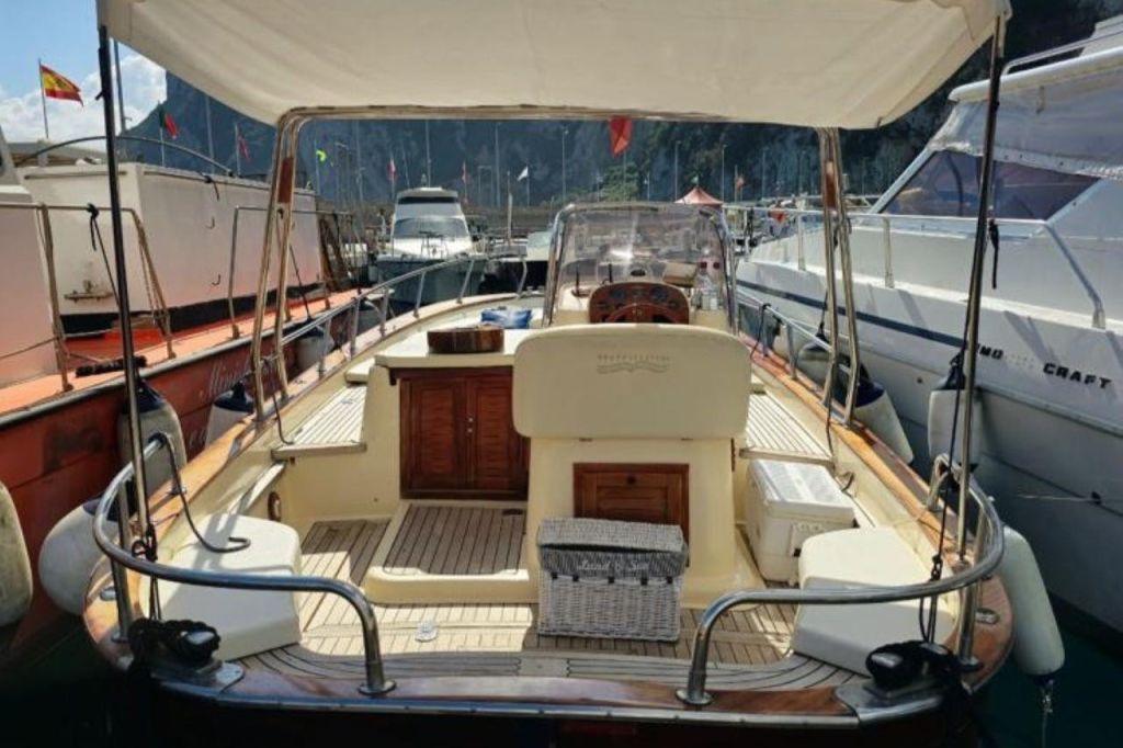 정박지에 정박한 모터보트의 뒷모습으로, 베이지색 인테리어와 캐노피, 주변 보트가 배경으로 펼쳐집니다.