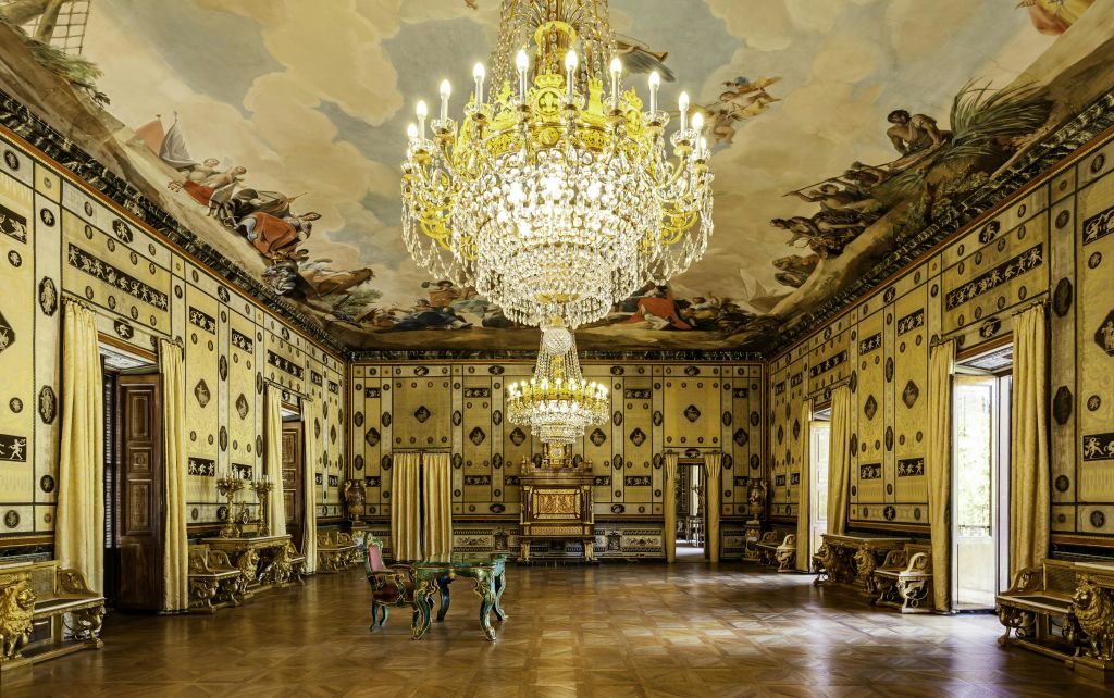 대형 샹들리에, 벽과 천장에 벽화, 앤티크 가구, 쪽모이 세공 마루가 있는 화려한 객실.