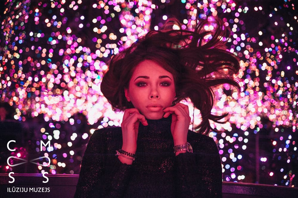 헝클어진 머리카락을 가진 여성이 화려한 보케 스타일 조명 앞에서 옷깃에 손을 얹은 채 포즈를 취하고 있습니다.