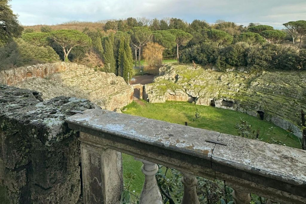 바위 지층과 나무, 흐린 하늘 아래 통로가 있는 푸르른 풍경이 내려다보이는 석조 난간 전망.
