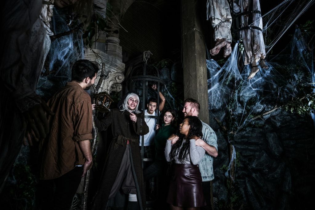 등불을 들고 있는 의상을 입은 사람과 거미줄이 가득한 으스스한 던전 주변에 서 있는 사람들.