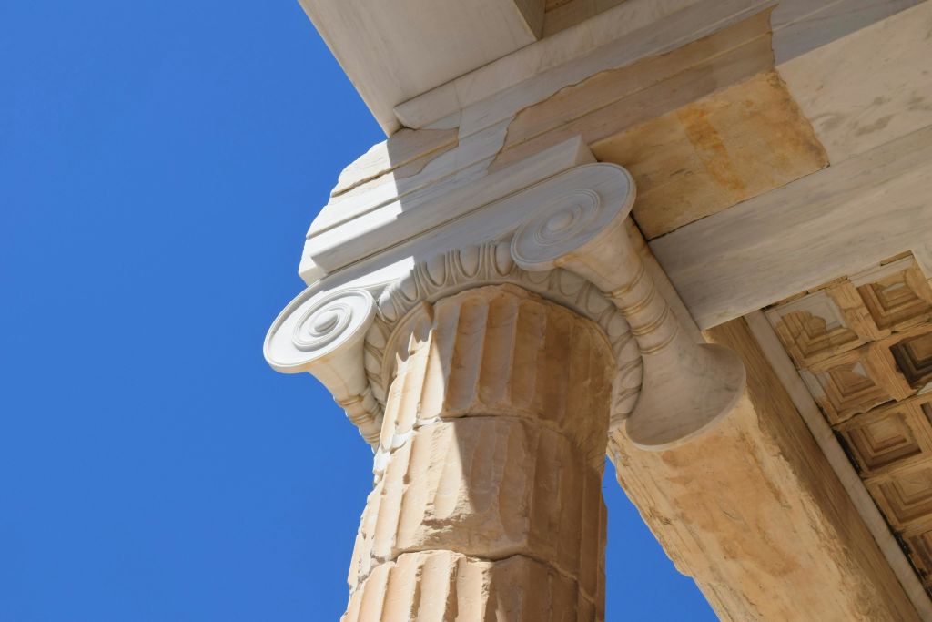 맑고 푸른 하늘 아래 고대 이오니아 기둥과 엔타블러처의 클로즈업.