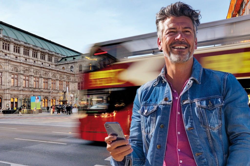 Fröhlicher Mann MIT Smartphone vor der Wiener Staatsoper, während ein Big Bus Sightseeing-Bus dynamisch vorbeifährt.