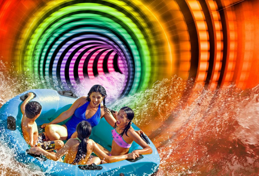 수영복을 입은 네 명의 사람이 파란색의 팽창식 뗏목을 타고 화려하고 나선형의 워터 슬라이드를 지나며 주변의 물을 튀깁니다.