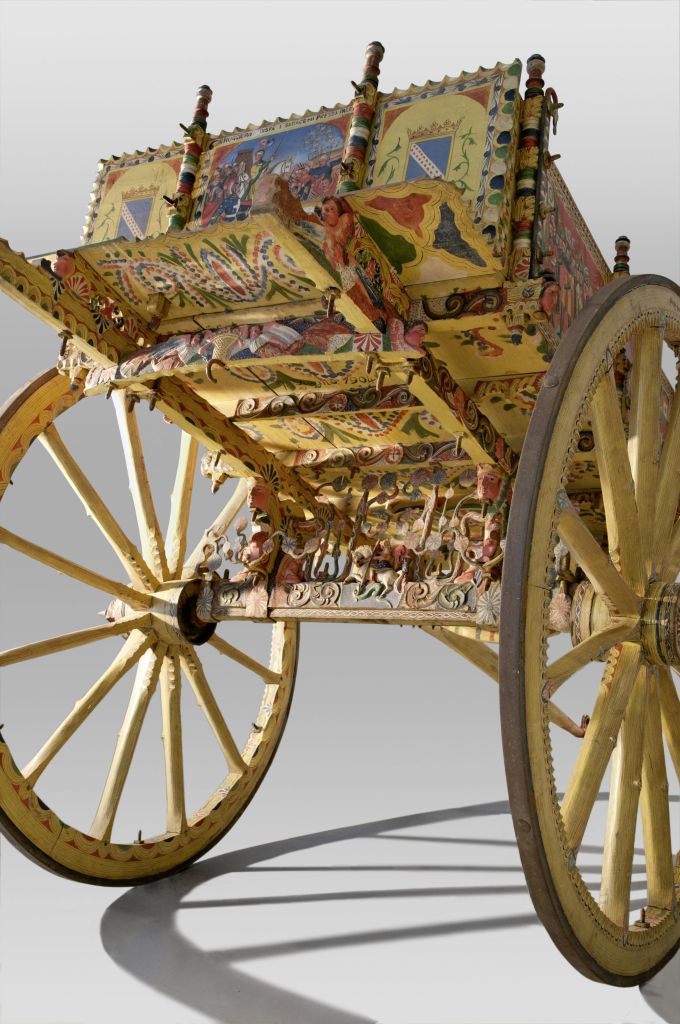 회색 배경에 페인트 장식과 커다란 스포크 바퀴가 있는 섬세하고 다채로운 앤티크 나무 카트입니다.