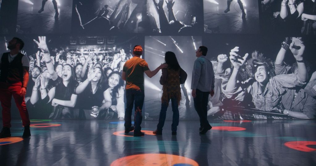 두 사람이 대형 스크린 앞에 서서 두 팔을 들어 올린 콘서트 관중의 흑백 사진을 전시하고 있습니다.