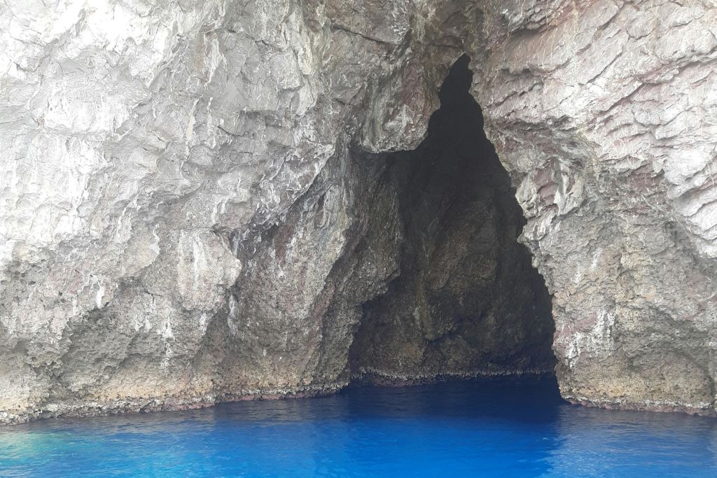 맑고 밝은 푸른 물에 부분적으로 잠긴 가장자리가 들쭉날쭉한 바위 동굴 입구.