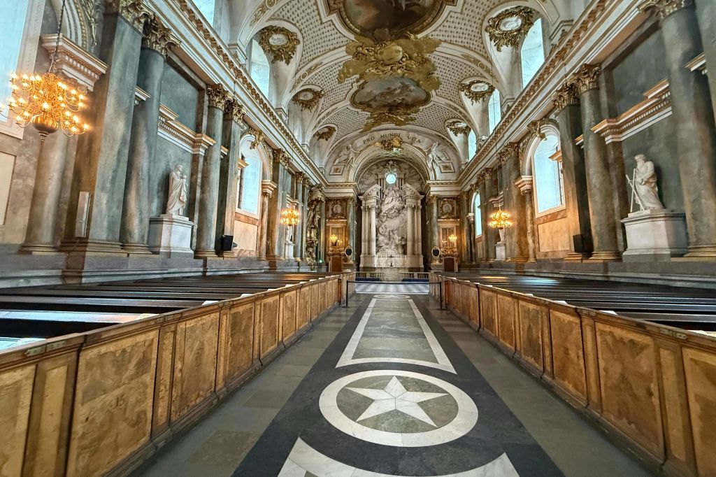 정교한 천장 디자인, 웅장한 기둥, 목조 퓨, 제단으로 이어지는 별 무늬 바닥이 있는 화려한 예배당 내부.