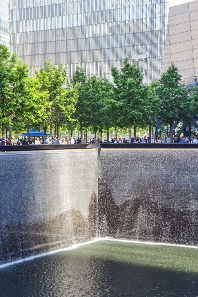 나무로 둘러싸인 커다란 기념 벽 아래로 물이 흘러내리고 수많은 사람들이 모여듭니다.