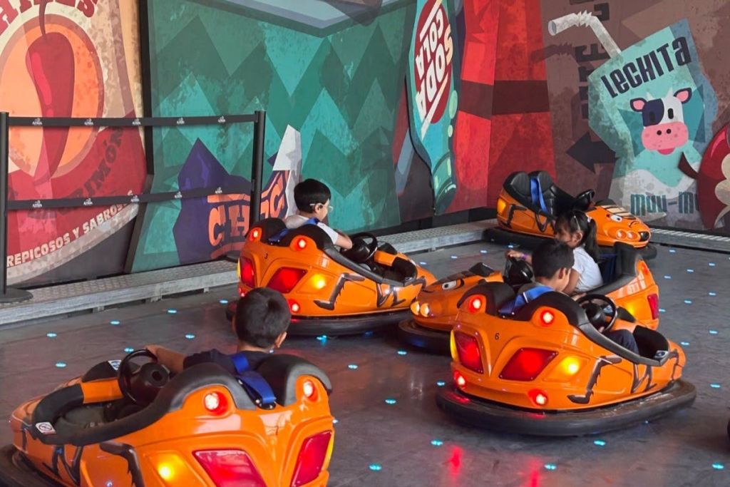 다채로운 벽화 배경이 있는 반사 바닥에서 아이들이 주황색 범퍼카를 타고 있습니다.