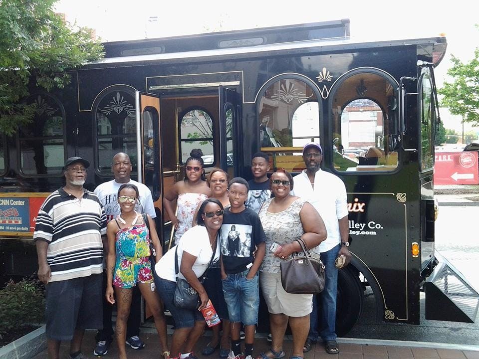 9명의 일행이 벽돌 거리에 주차된 검은색 전차 앞에 서서 미소를 짓고 있습니다.