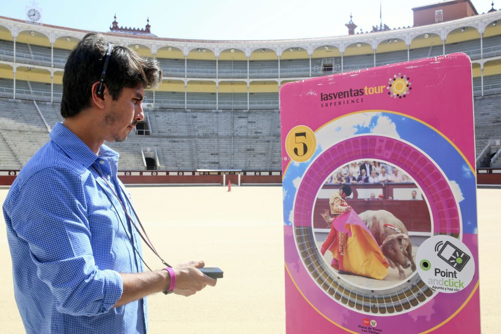 파란색 셔츠와 헤드셋을 착용한 남성이 햇빛이 비어 있는 경기장에서 양궁 대상을 바라보고 있습니다.