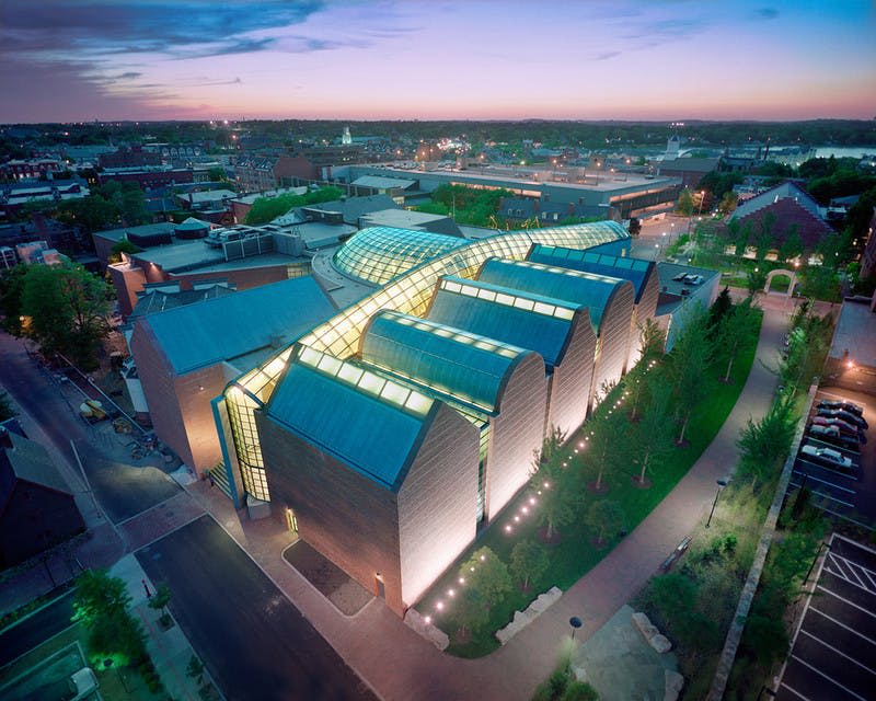 도시 풍경과 녹지로 둘러싸인 황혼의 곡선형 조명 유리 지붕이 있는 현대적인 건물의 공중 전망.