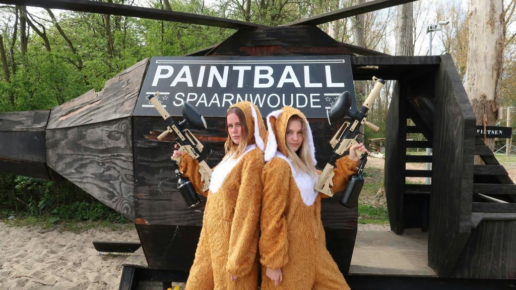 갈색 동물 복장을 한 두 사람이 야외에서 'PAINTBALL SPAARNWOUDE' 표지판 앞에서 페인트볼 총을 들고 있습니다.