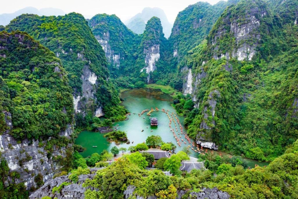 높은 카르스트 언덕으로 둘러싸인 푸른 계곡으로, 보트가 있는 강과 물 위의 작은 파빌리온이 특징입니다.