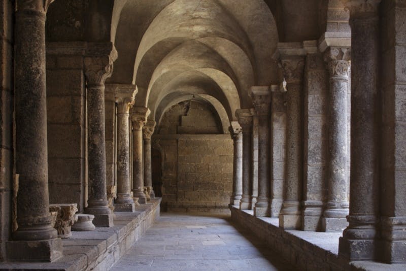 고대 또는 유서 깊은 건물로 보이는 기둥으로 지탱되는 아치형 천장이 있는 석조 복도.
