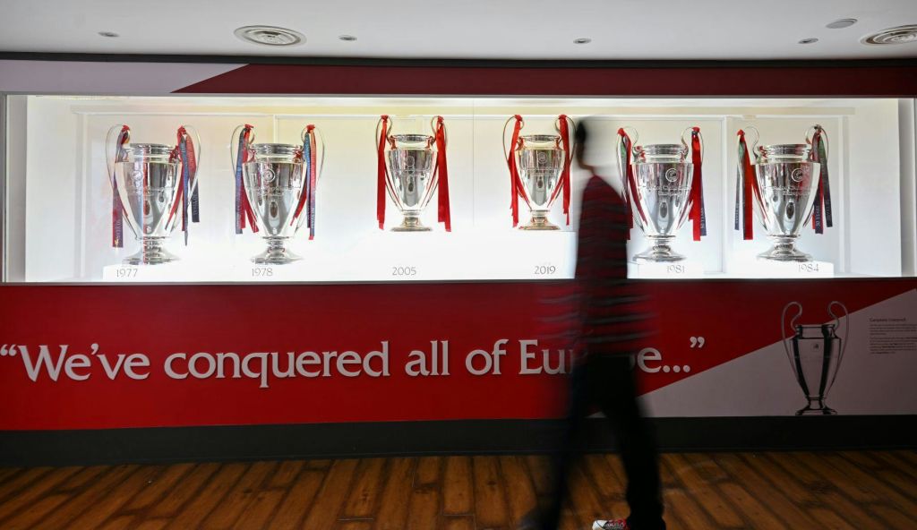 한 사람이 빨간색과 흰색 벽에 빨간색 리본이 달린 5개의 은색 트로피를 지나가고 있습니다.