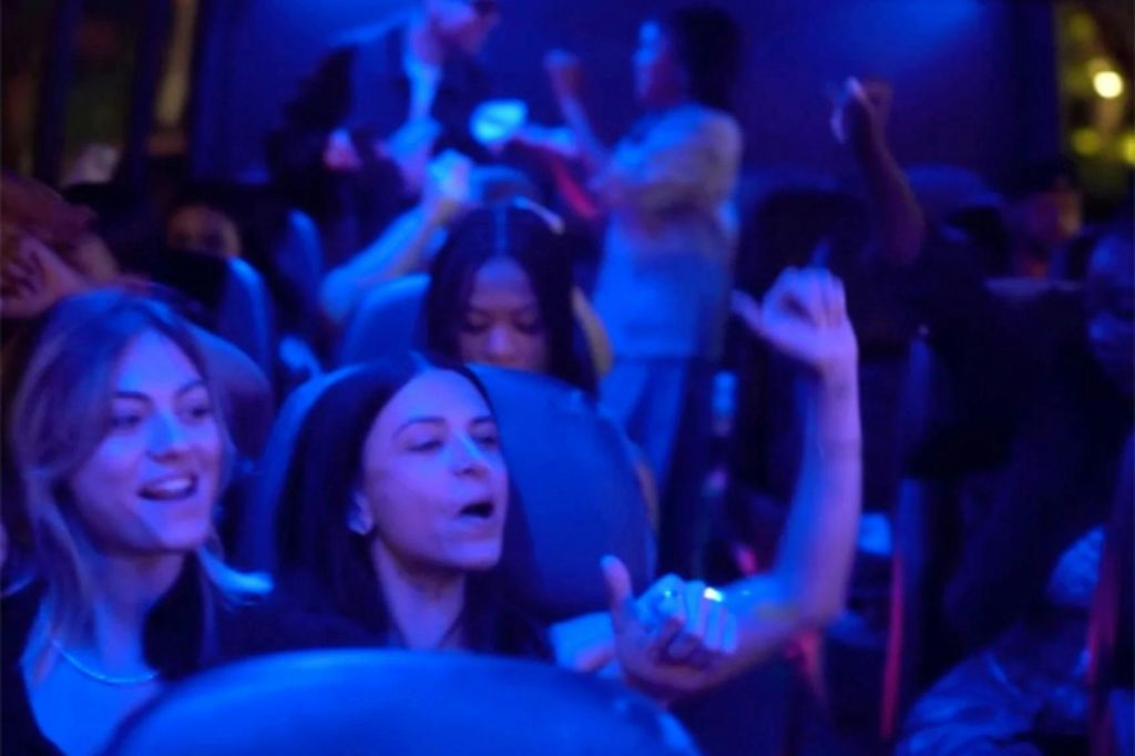 파란색 불빛이 비추는 버스나 기차에 탄 사람들이 말을 걸고 라이딩을 즐기는 것처럼 보입니다.