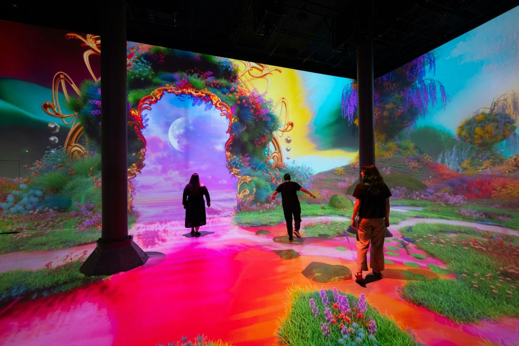 화려한 디지털 풍경과 기발한 아치형 통로가 있는 밝은 조명의 몰입형 예술 작품에 참여하는 사람들.