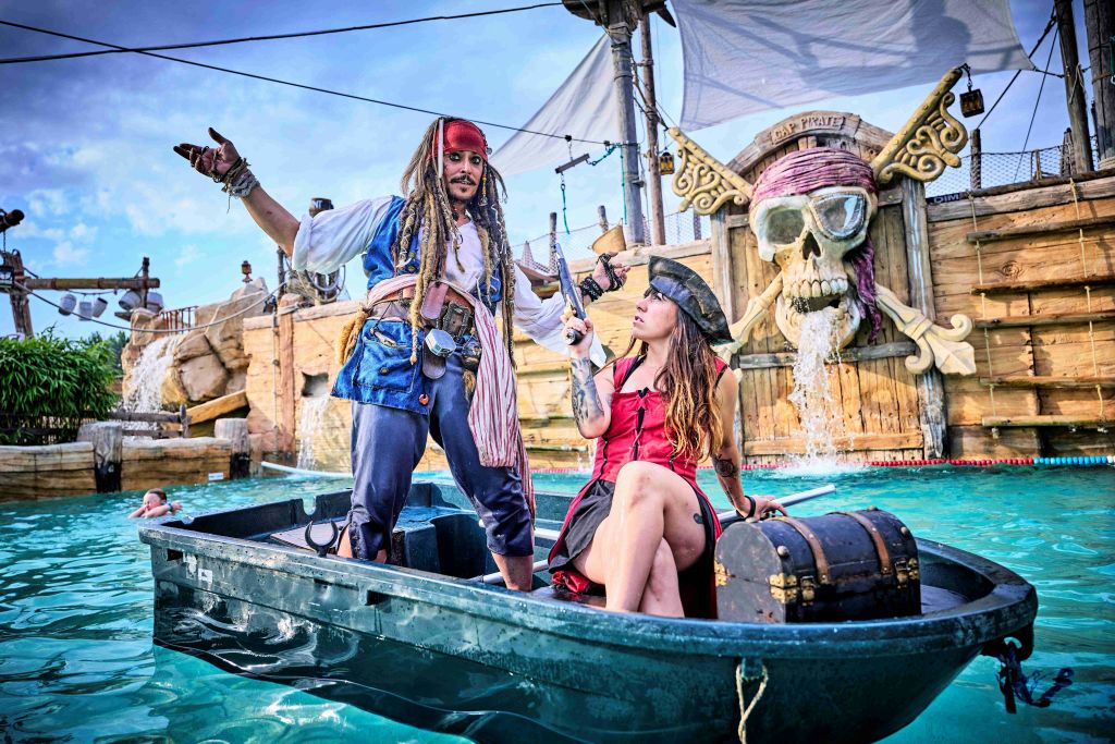 커다란 해골 장식을 배경으로 테마가 있는 수상 어트랙션에서 작은 보트를 타고 해적 의상을 입은 두 사람.