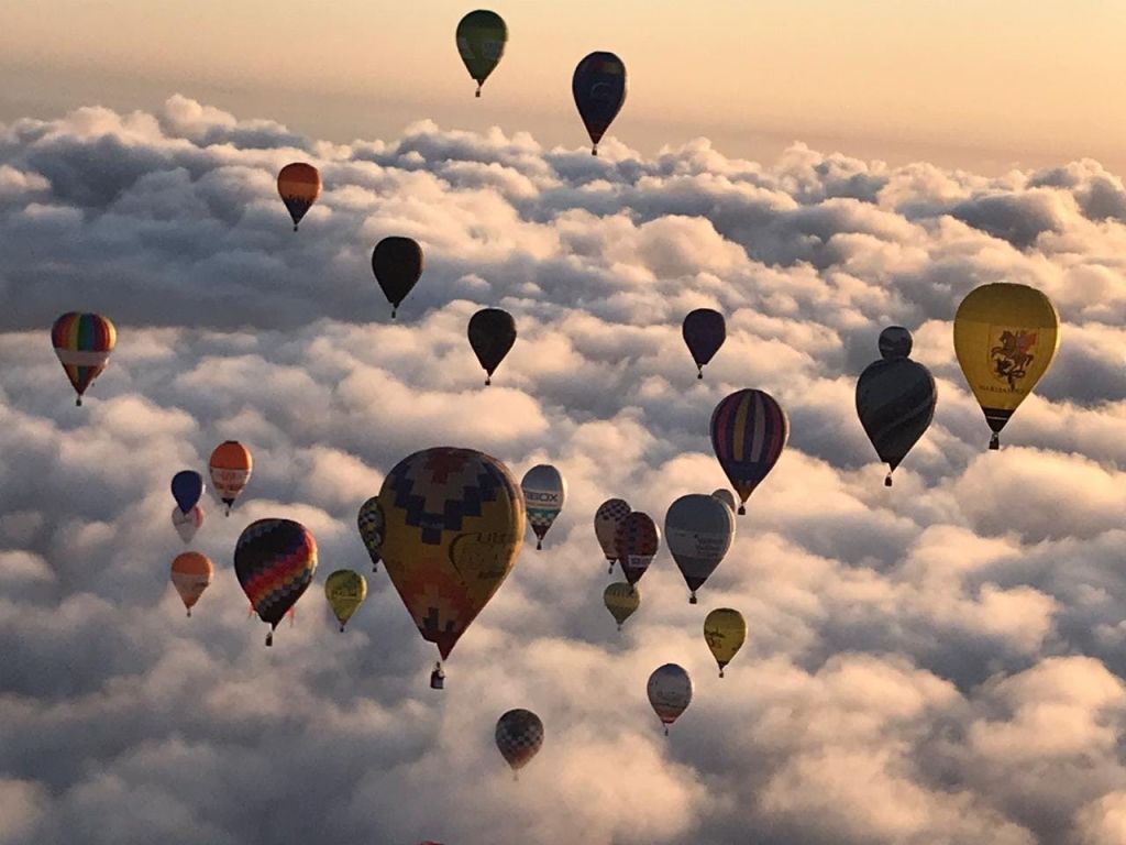 해가 뜨거나 지는 동안 수많은 다채로운 열기구가 구름 바다 위에 떠 있습니다.